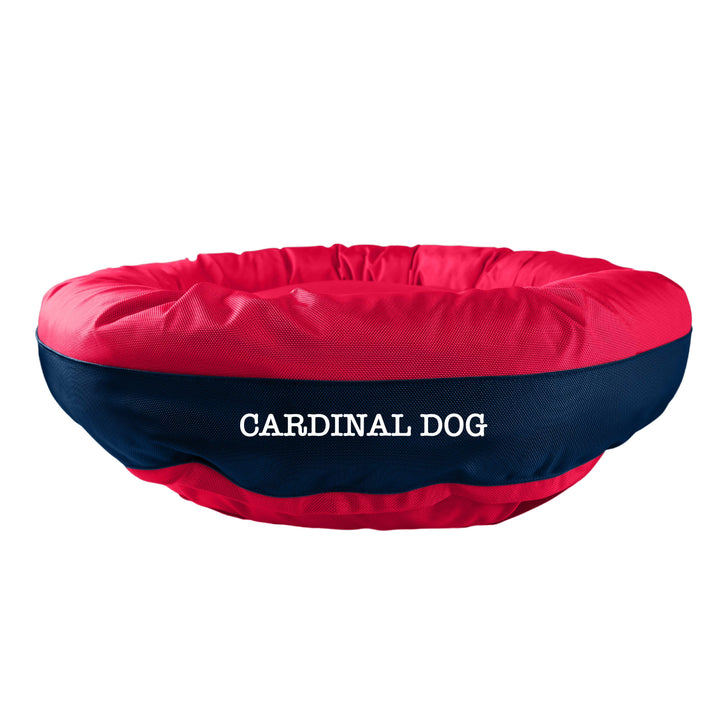 Blue round bolstered dog bed with a red band in the middle with white embroidered 'Carinal Dog'.