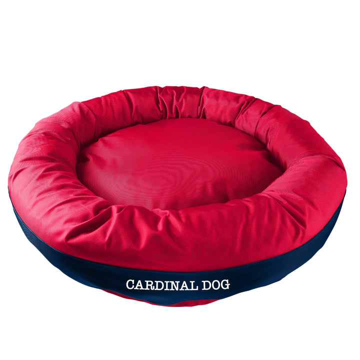 Blue round bolstered dog bed with a red band in the middle with white embroidered 'Carinal Dog'.