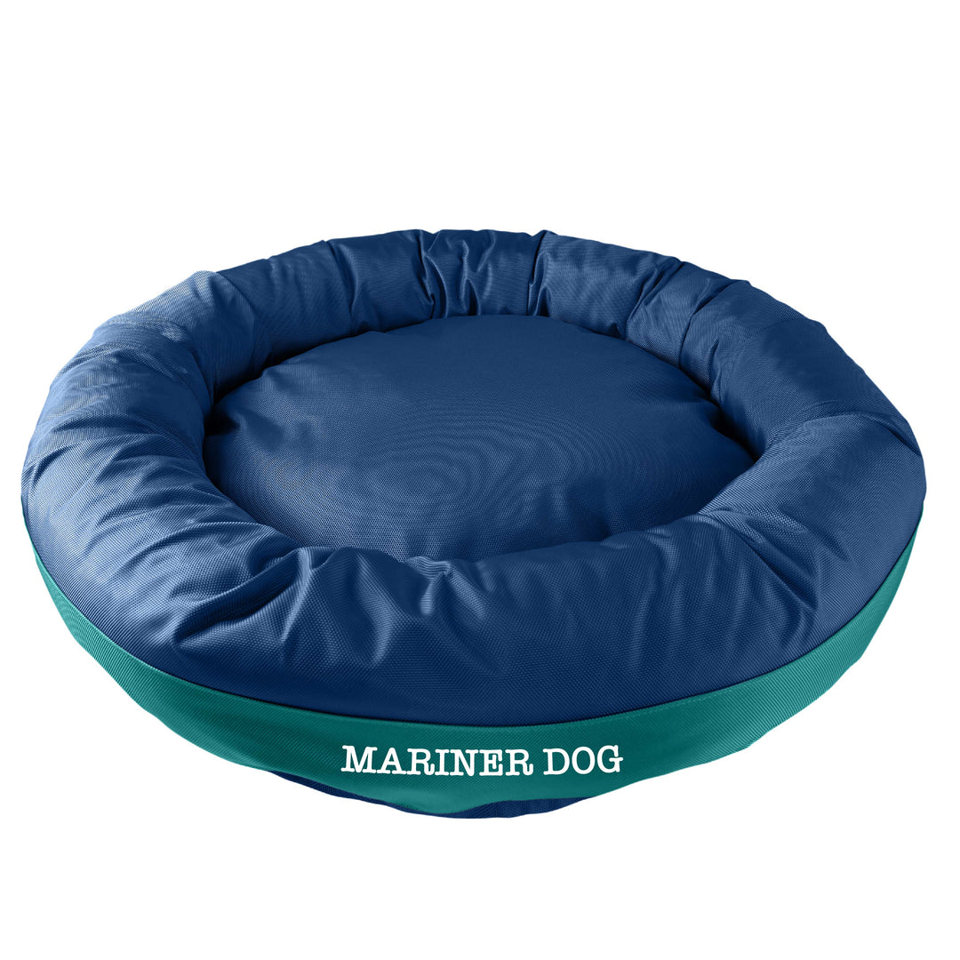 Navy round bolstered dog bed with a teal band and white embroidered 'Mariner Dog'.  Edit alt text