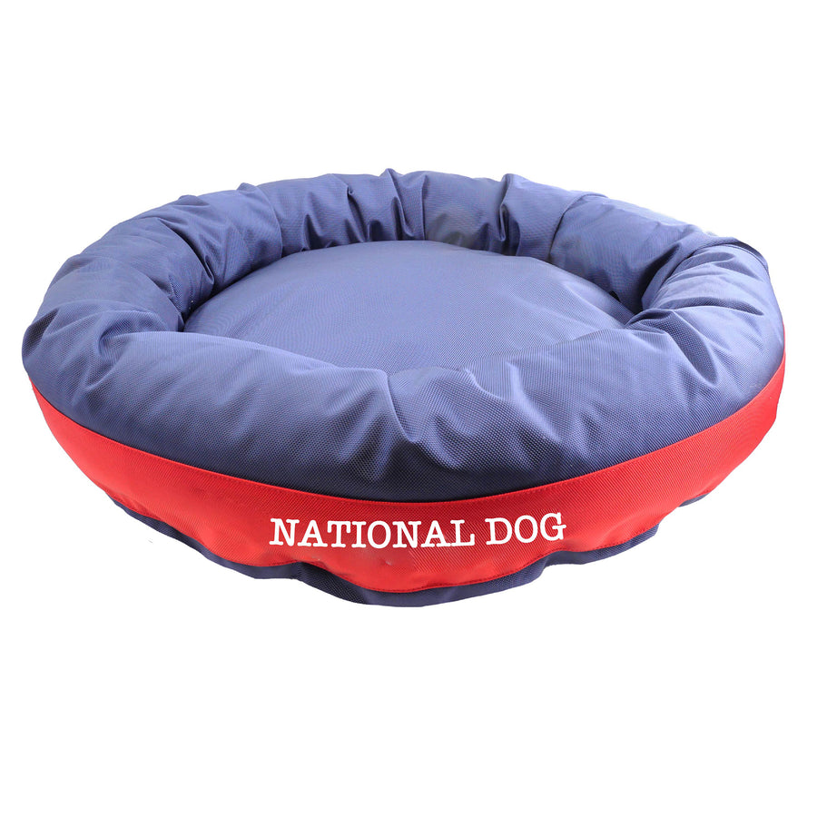 Navy round bolstered dog bed with red band and white embroidered 'National Dog'.