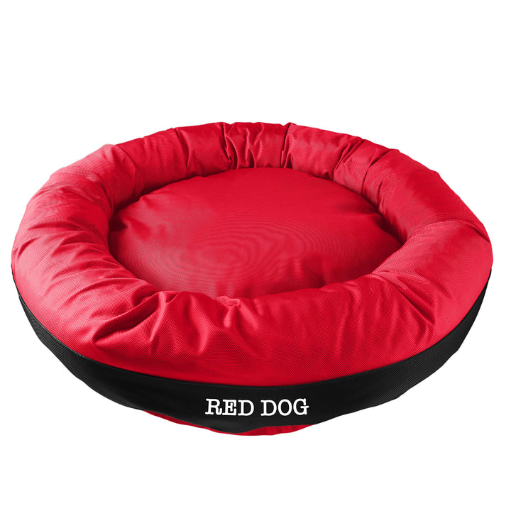 Red round bolstered dog bed with a black band and white embroidered 'Red Dog'.